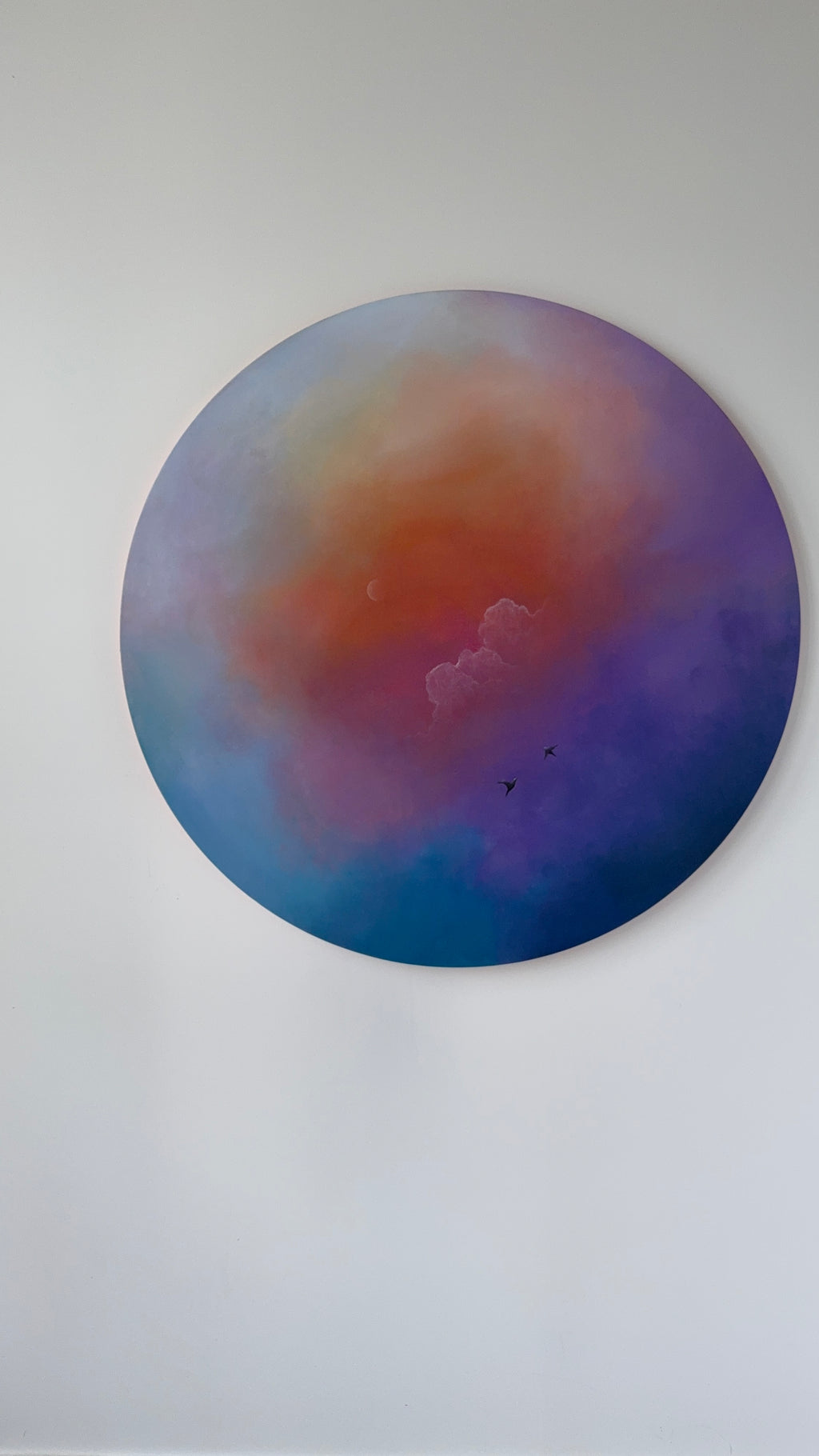 Round abstract painting with a gradient of blue, purple, and orange on a white wall.